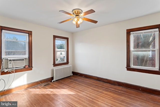 empty room featuring ceiling fan, radiator, wood-type flooring, and cooling unit