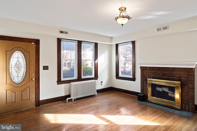 foyer entrance with radiator heating unit, a fireplace, and hardwood / wood-style floors