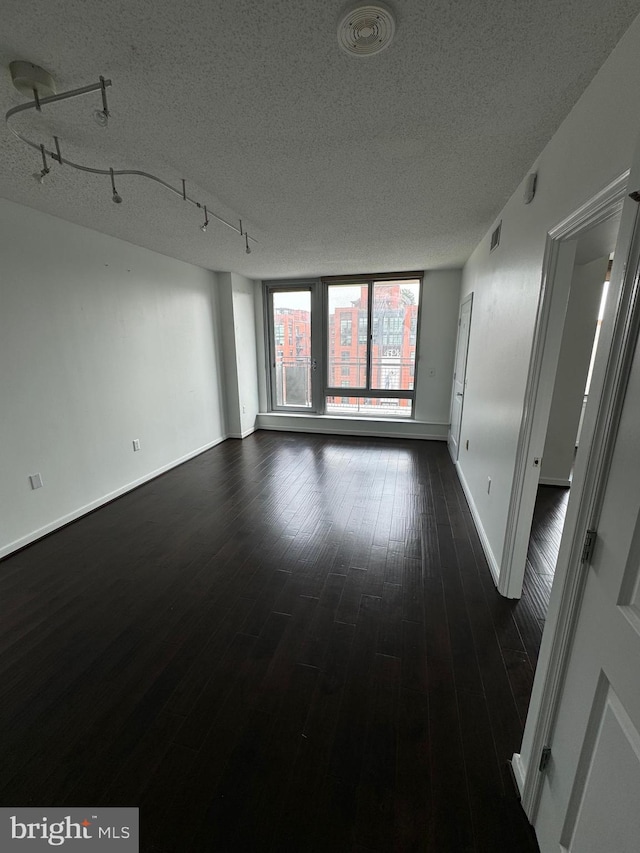 empty room featuring a textured ceiling, dark wood-style flooring, visible vents, baseboards, and rail lighting