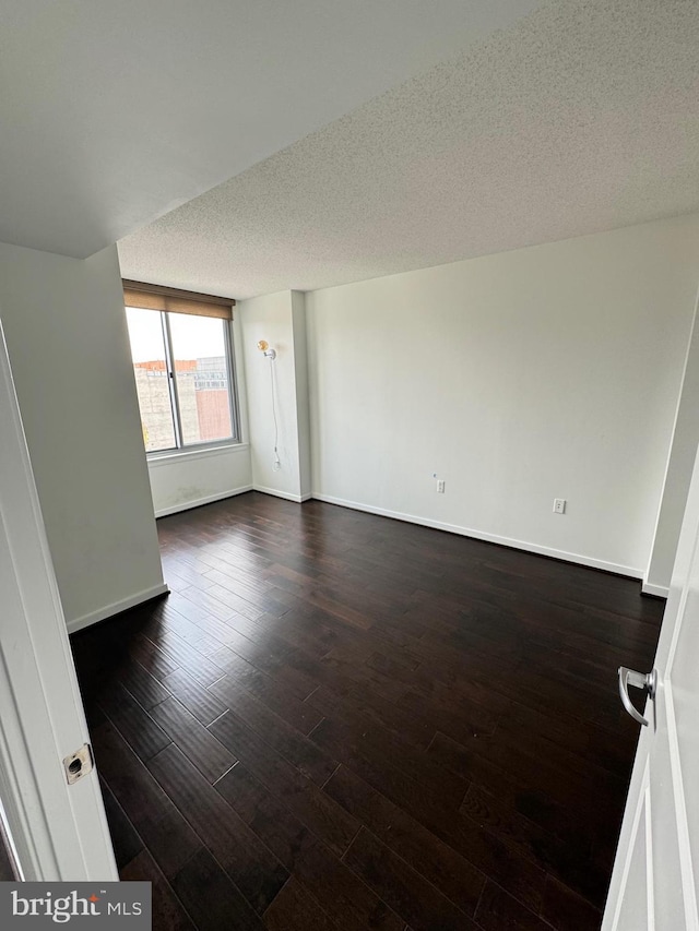 empty room featuring dark wood finished floors, a textured ceiling, and baseboards