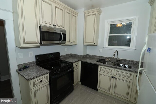 kitchen with sink, dark stone countertops, cream cabinets, light tile patterned floors, and black appliances