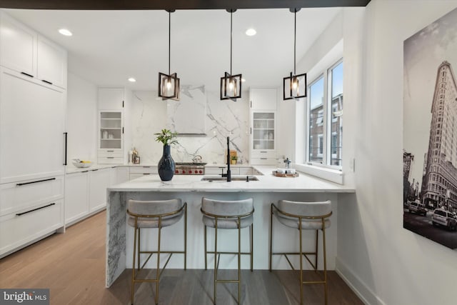 kitchen featuring light wood-type flooring, white cabinetry, a kitchen breakfast bar, backsplash, and decorative light fixtures