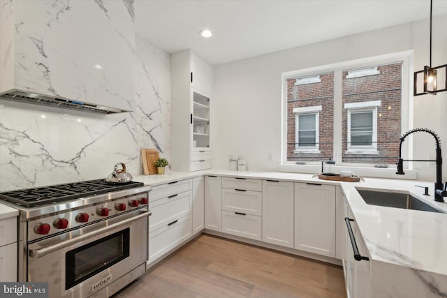 kitchen with light hardwood / wood-style flooring, white cabinets, hanging light fixtures, and designer stove