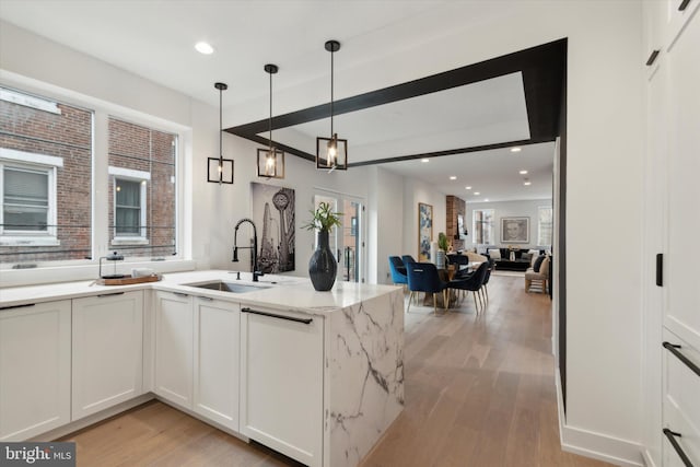 kitchen featuring pendant lighting, light hardwood / wood-style floors, sink, white cabinets, and kitchen peninsula