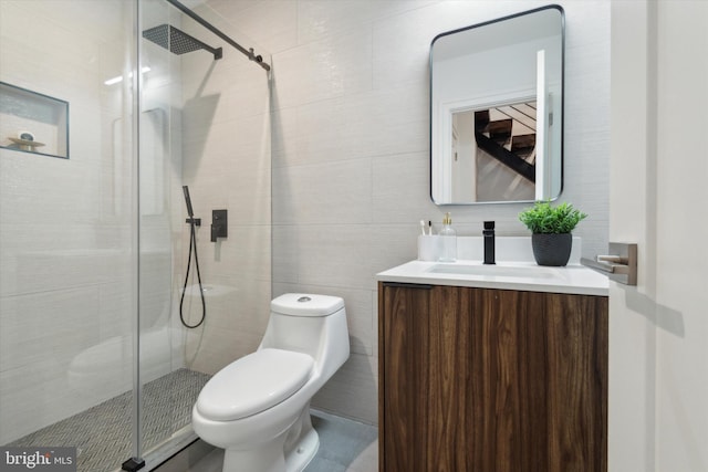 bathroom with tile walls, a shower with shower door, vanity, and toilet