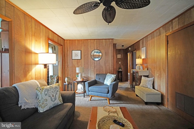 carpeted living room featuring wood walls, visible vents, a ceiling fan, and ornamental molding