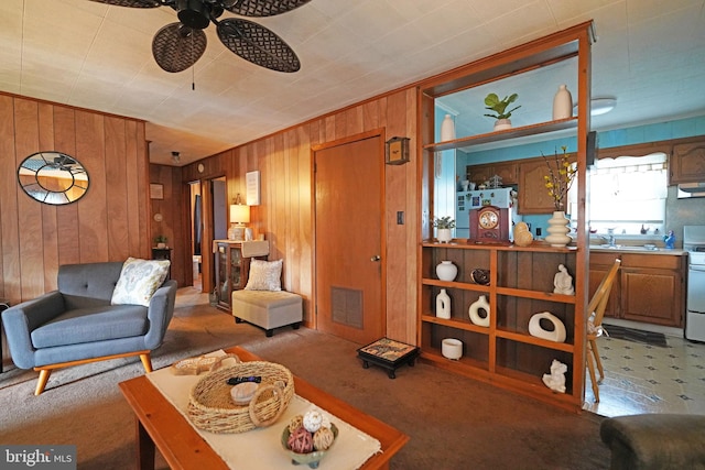 living room featuring ceiling fan, carpet flooring, wood walls, and sink