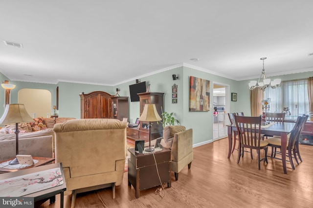 living room with visible vents, ornamental molding, wood finished floors, baseboards, and a chandelier