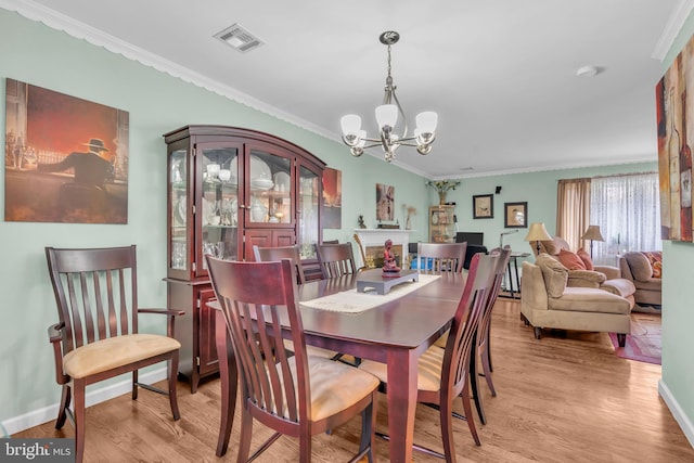 dining area with a notable chandelier, visible vents, light wood-type flooring, and ornamental molding