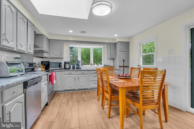 kitchen with a wealth of natural light, stainless steel appliances, gray cabinetry, and visible vents