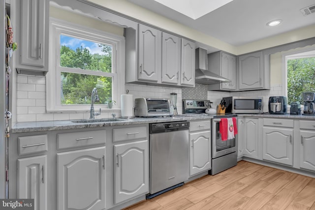 kitchen with a sink, appliances with stainless steel finishes, wall chimney exhaust hood, a toaster, and a healthy amount of sunlight