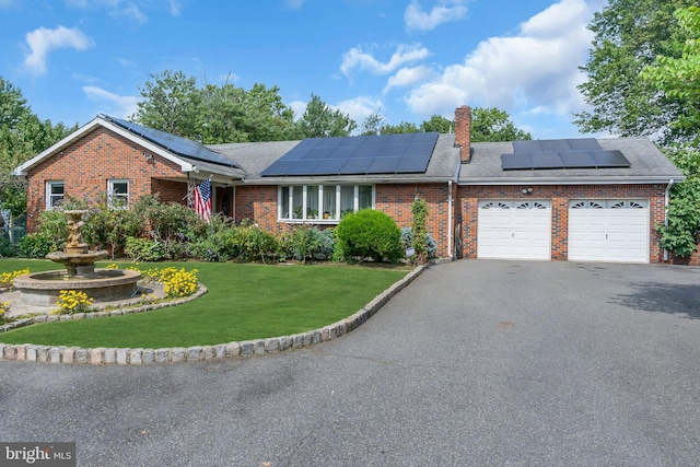 ranch-style home with solar panels, a garage, and a front lawn