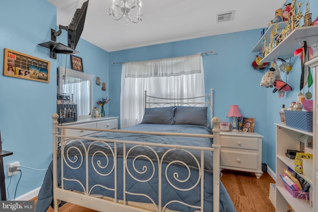 bedroom with visible vents, baseboards, a notable chandelier, and wood finished floors