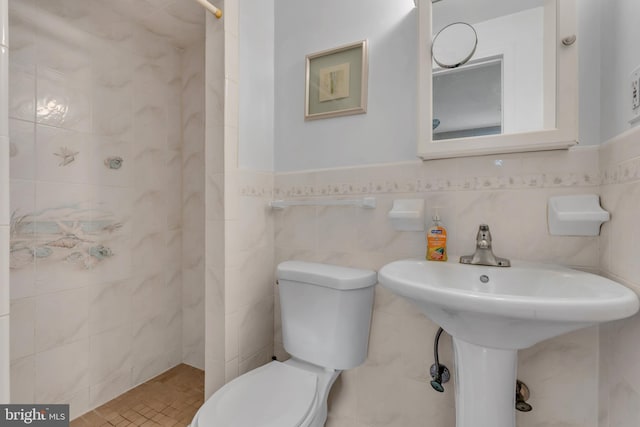 full bathroom featuring tile walls, toilet, a wainscoted wall, and a tile shower