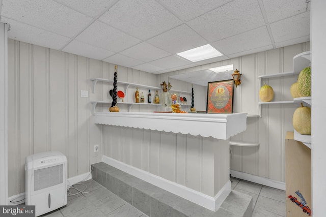 bar featuring tile patterned floors, a drop ceiling, a bar, and a decorative wall