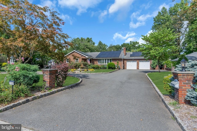 ranch-style home with brick siding, aphalt driveway, a front yard, roof mounted solar panels, and a garage