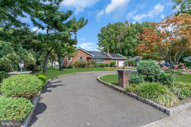 ranch-style house with a front lawn, driveway, an attached garage, brick siding, and a chimney