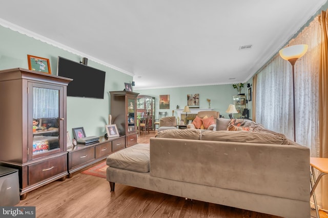 living area with visible vents, wood finished floors, and ornamental molding