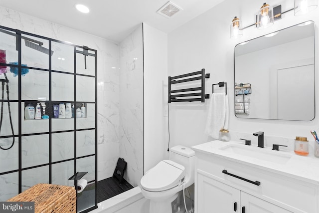 bathroom with a tile shower, vanity, and toilet