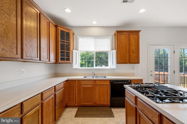 kitchen featuring a sink, light countertops, brown cabinets, black appliances, and glass insert cabinets