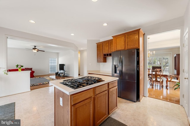 kitchen featuring light hardwood / wood-style floors, stainless steel gas stovetop, ceiling fan with notable chandelier, black fridge with ice dispenser, and a center island