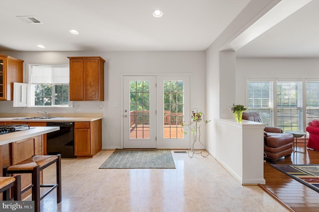 kitchen with black dishwasher, brown cabinets, light countertops, visible vents, and glass insert cabinets