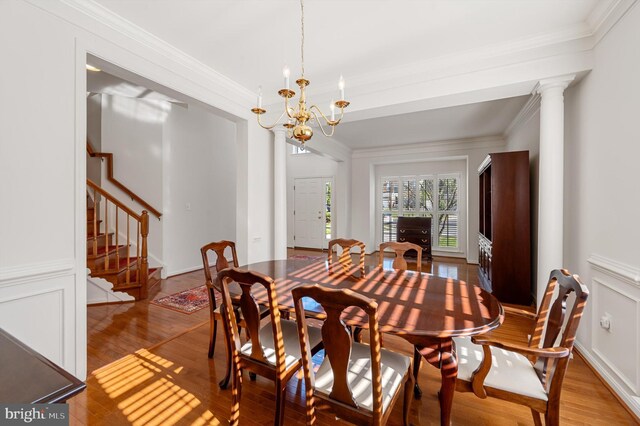 dining area with hardwood / wood-style flooring, decorative columns, a notable chandelier, and crown molding