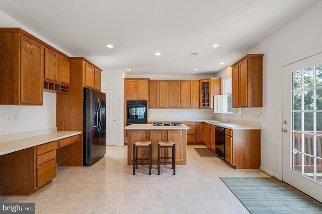 kitchen featuring a breakfast bar area, a center island, light countertops, brown cabinets, and black appliances