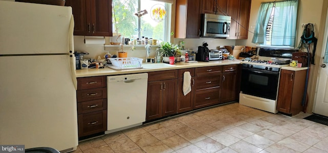 kitchen with sink, dark brown cabinetry, white appliances, and light tile patterned floors