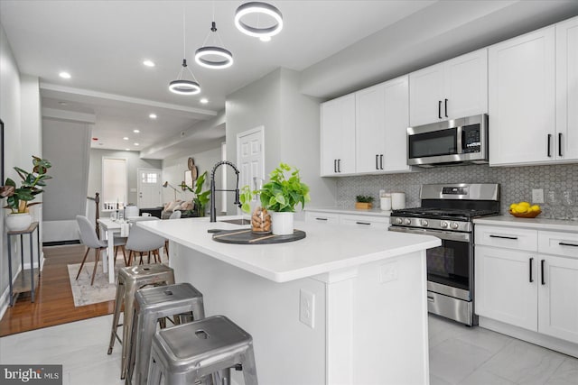 kitchen featuring appliances with stainless steel finishes, light hardwood / wood-style flooring, decorative backsplash, an island with sink, and hanging light fixtures