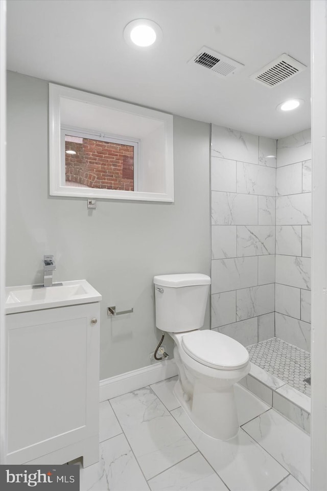 bathroom featuring toilet, vanity, tiled shower, and tile patterned floors