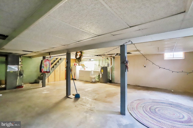 basement with water heater, separate washer and dryer, heating unit, and a drop ceiling