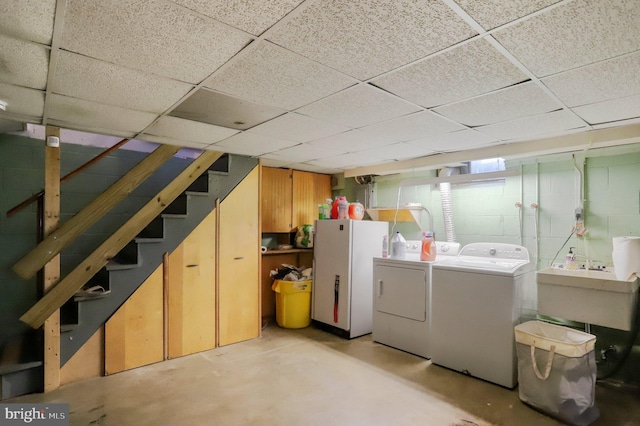 basement featuring washing machine and clothes dryer, a paneled ceiling, and white fridge