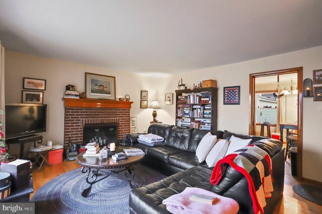 living room with a notable chandelier, a brick fireplace, and hardwood / wood-style floors