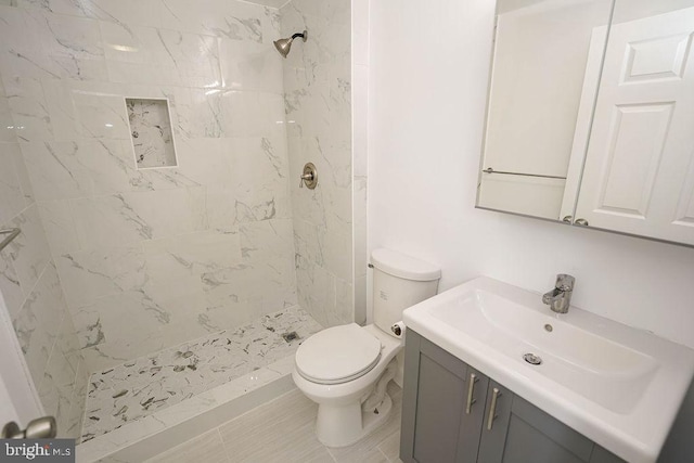 bathroom with tile patterned flooring, toilet, a tile shower, and vanity