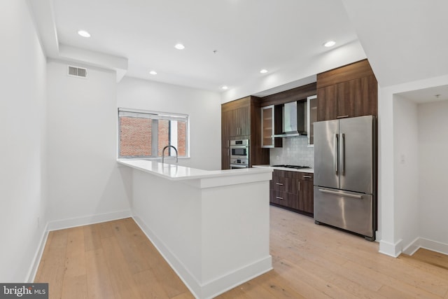 kitchen featuring wall chimney exhaust hood, light hardwood / wood-style flooring, appliances with stainless steel finishes, tasteful backsplash, and sink