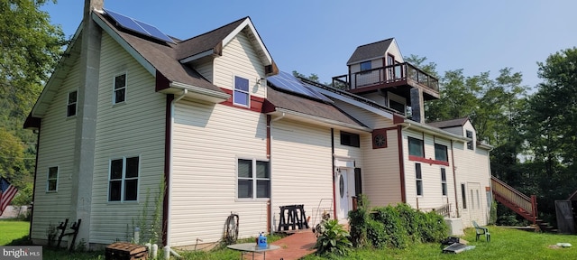 back of property featuring a yard, a balcony, and solar panels