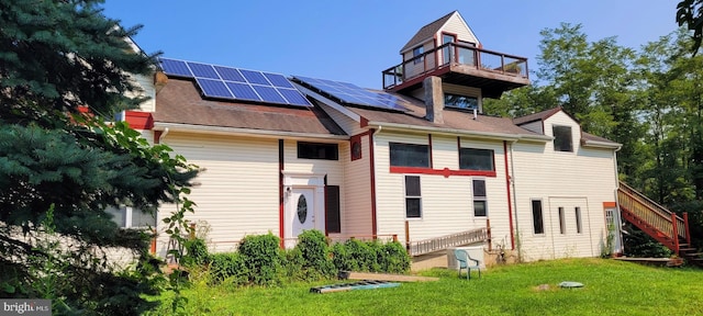 rear view of house featuring solar panels, a balcony, and a yard