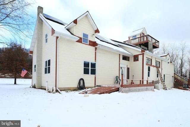 snow covered rear of property with solar panels, a balcony, and a wooden deck