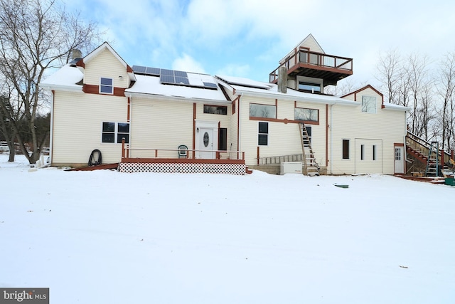 snow covered back of property featuring solar panels and a deck