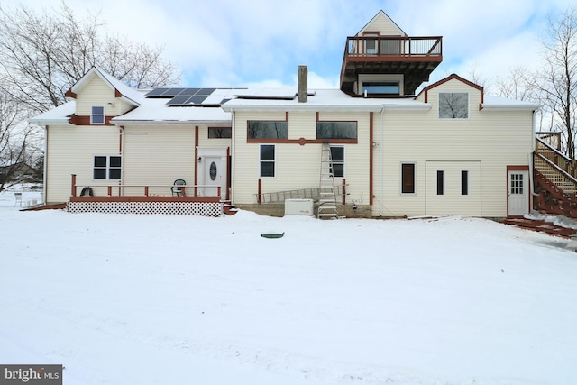 snow covered property with a wooden deck and solar panels