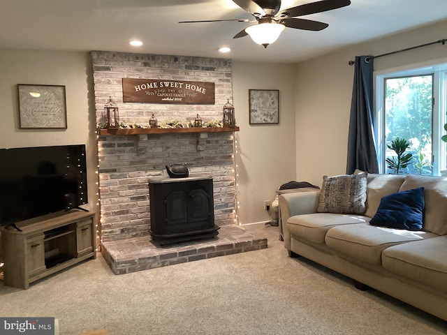 living room with a wood stove, ceiling fan, carpet floors, and a fireplace