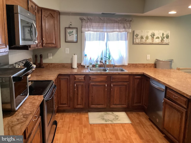 kitchen with light hardwood / wood-style floors, appliances with stainless steel finishes, sink, and kitchen peninsula