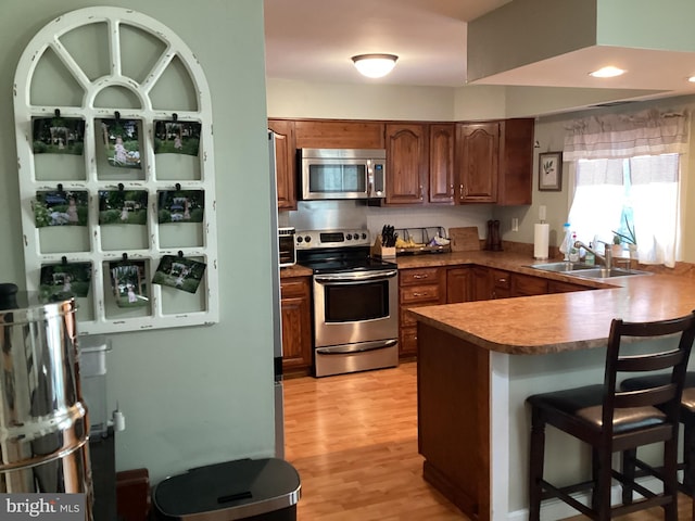 kitchen with sink, kitchen peninsula, appliances with stainless steel finishes, a breakfast bar area, and light wood-type flooring