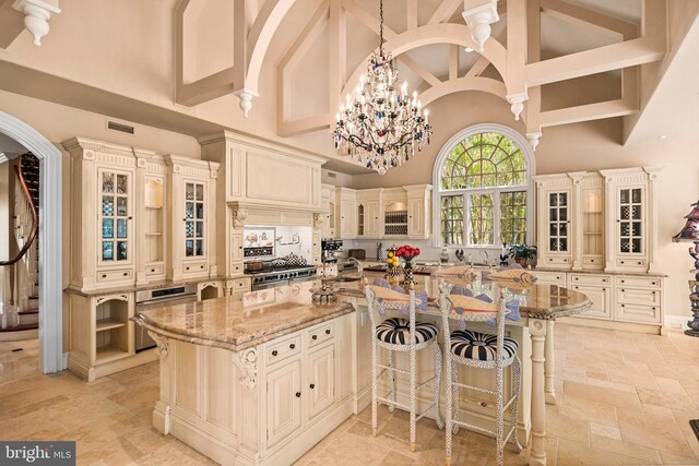 kitchen featuring a large island with sink, high vaulted ceiling, hanging light fixtures, cream cabinets, and light tile patterned floors