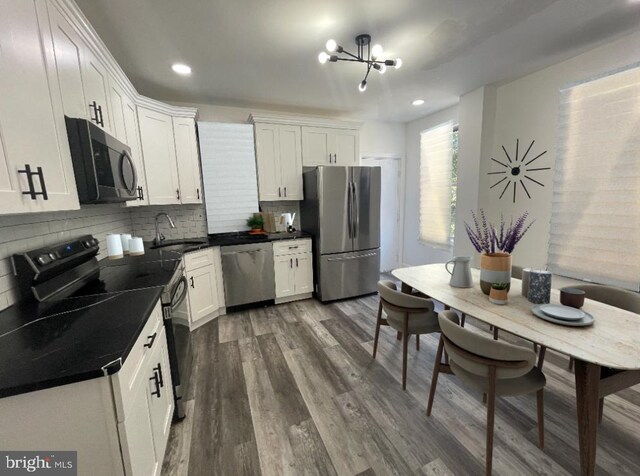 kitchen featuring appliances with stainless steel finishes, dark hardwood / wood-style flooring, a chandelier, white cabinetry, and decorative backsplash