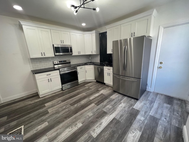 kitchen with dark wood finished floors, dark countertops, decorative backsplash, appliances with stainless steel finishes, and white cabinetry