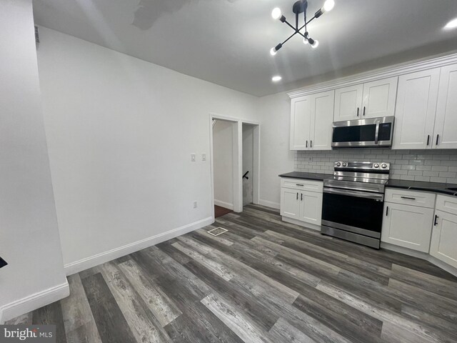 kitchen featuring white cabinets, appliances with stainless steel finishes, backsplash, dark countertops, and dark wood finished floors