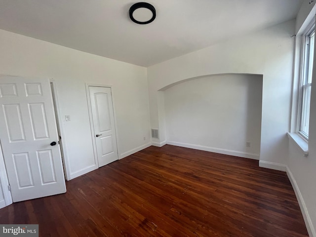 spare room with baseboards, visible vents, arched walkways, and wood finished floors