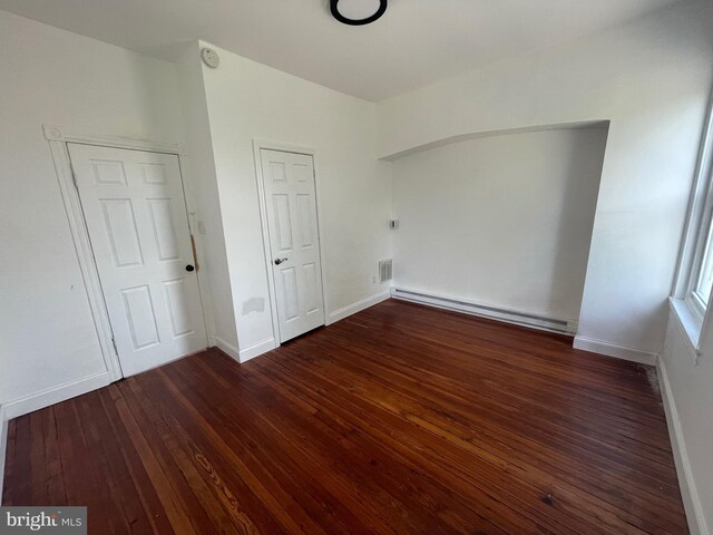 unfurnished bedroom with a baseboard heating unit, visible vents, hardwood / wood-style flooring, and baseboards